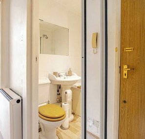 A compact bathroom with a toilet, sink, and mirror, featuring a towel dispenser and a wooden door with a brass handle.