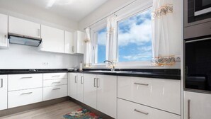 Una cocina moderna con armarios blancos, encimeras negras, una alfombra colorida y un ventanal con cortinas.