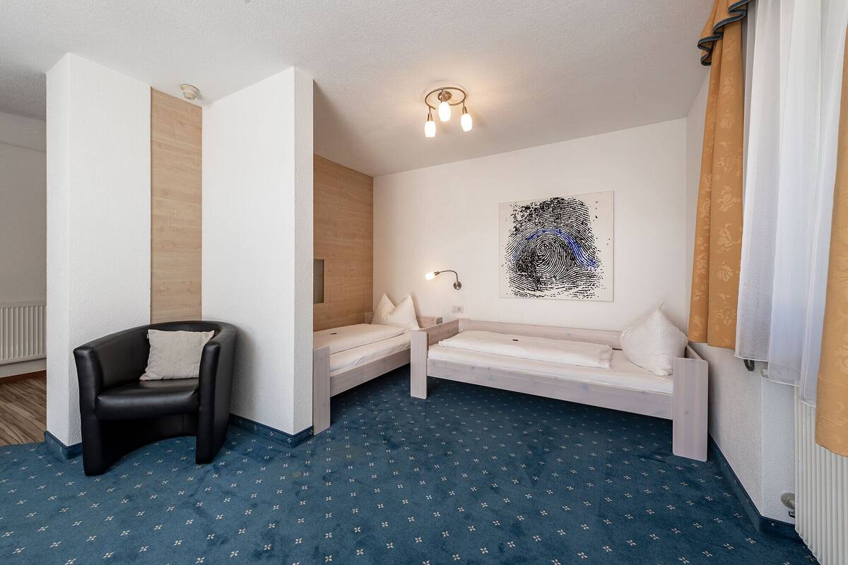 A room with a black leather chair, a white sofa, a small bed, and a wall-mounted light fixture.