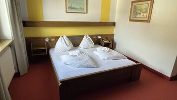Une chambre d’hôtel avec un lit, une table de chevet, une commode, une fenêtre et deux tableaux encadrés au mur.