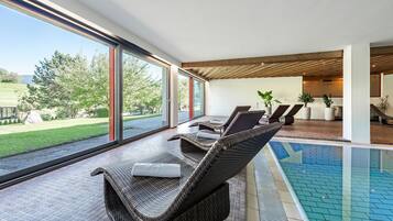 Un área de piscina interior moderna con sillones de mimbre y vistas al exterior.