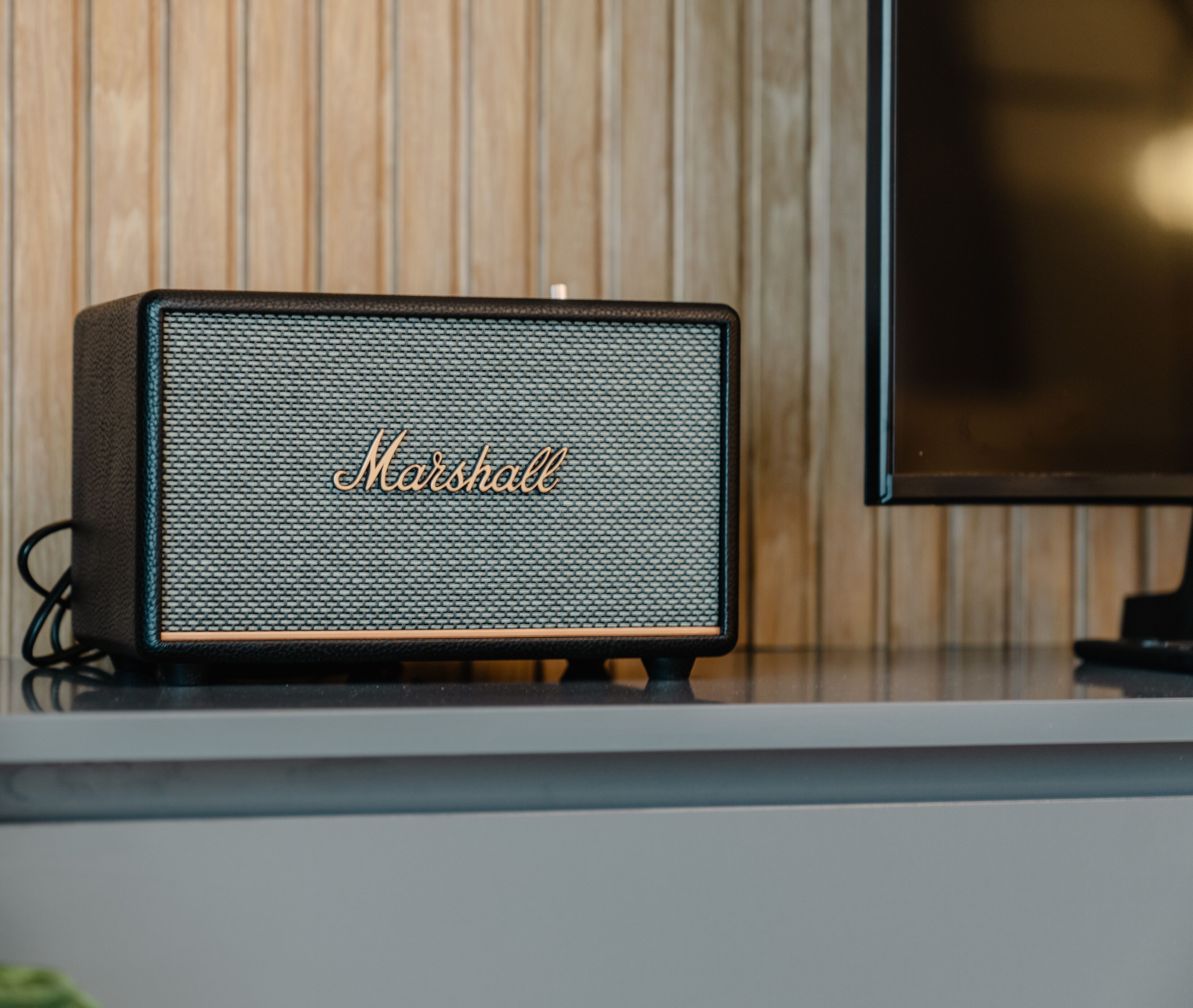 A Marshall speaker on a white surface with a wooden panel background.