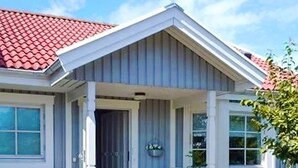 Une maison avec un toit recouvert de tuiles rouges, une véranda avec deux chaises et une fenêtre avec un rideau.