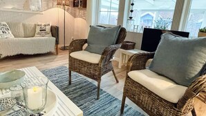 Un salon chaleureux avec des fauteuils en osier, un canapé blanc et une table en verre agrémentée d’objets décoratifs.