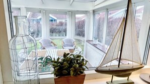 Une véranda donnant sur un jardin, une maquette de voilier et une bouteille en verre avec une cage en fil de fer.