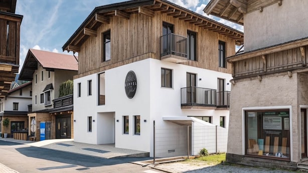 A modern building with a wooden facade, a balcony, and a circular logo on the front. - Apartment in Kirchberg Near Ski Lift (Kirchberg in Tirol)