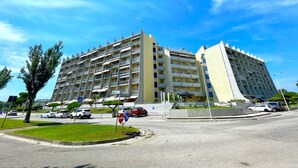 A multi-story hotel with a modern architectural design, featuring balconies on each floor, a parking area in front, and a clear blue sky in the background. - Apartment in Porto Santa Margherita Near Beach (Caorle)