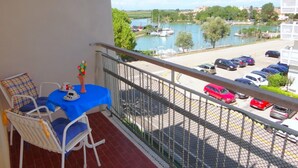 A balcony with a table and chairs, overlooking a parking area and a body of water with boats. - Apartment in Porto Santa Margherita Near Beach (Caorle)