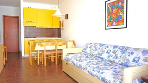 A compact living space with a kitchenette, a dining area, and a sofa. - Apartment in Porto Santa Margherita Near Beach (Caorle)