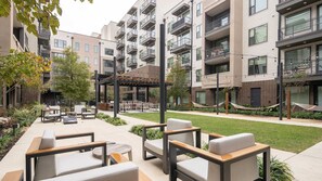 Un patio con mobiliario exterior, una pérgola y un edificio de ladrillo con balcones.