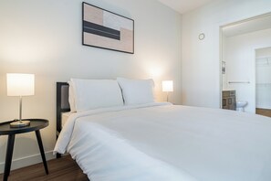Una cama bien hecha con sábanas blancas, dos lámparas de noche y un cuadro abstracto moderno en la pared.