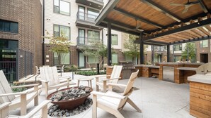 An outdoor patio with wooden chairs, a fire pit, and a grill area. - Westerly (Dallas)