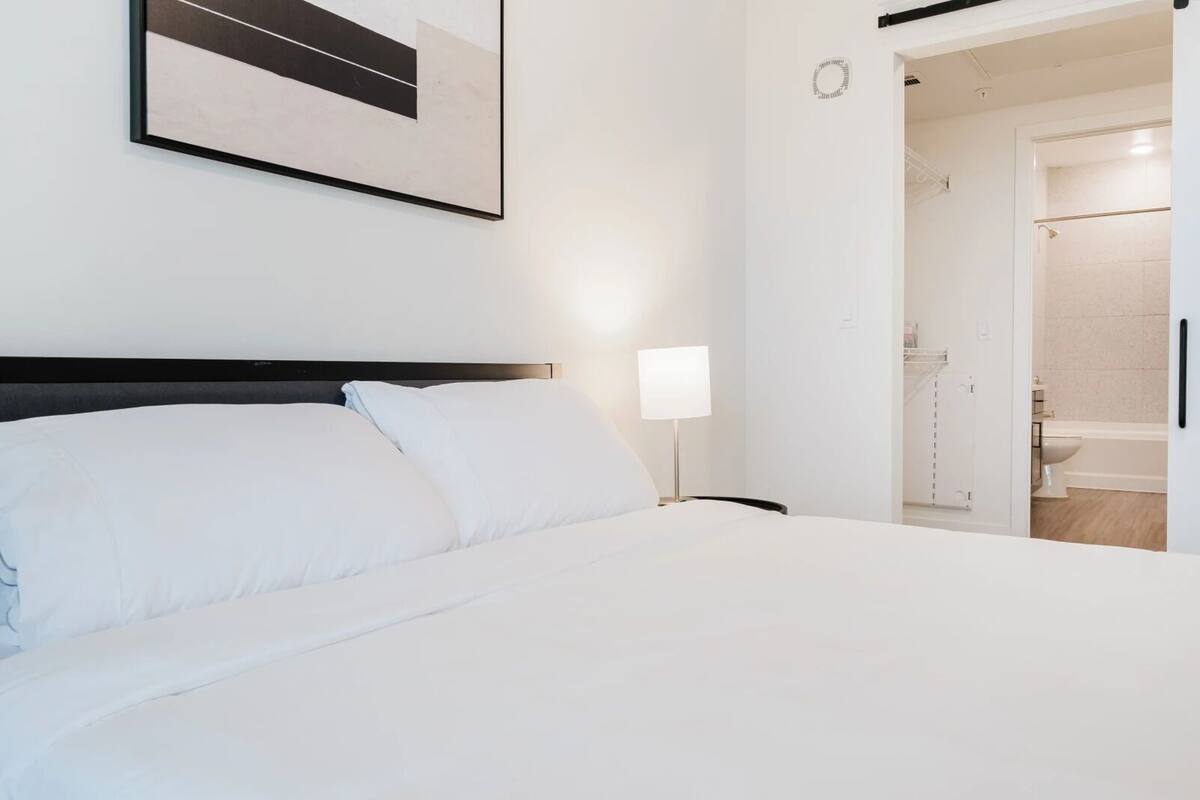 A hotel room with a bed, a nightstand, a lamp, and a door leading to a bathroom.