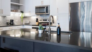 A modern kitchen with white cabinets, stainless steel appliances, and a central island with a sink and a potted plant. - Westerly (Dallas)