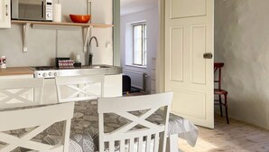 A compact kitchen with a microwave, stove, and sink. There's a dining area with a table and chairs. A red chair is visible in the corner. - 5 Person Holiday Home in Stenkyrka (Tingstade)