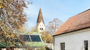 A church with a tall spire, a building with a red roof, and a tree with autumn leaves. - 5 Person Holiday Home in Stenkyrka (Tingstade)
