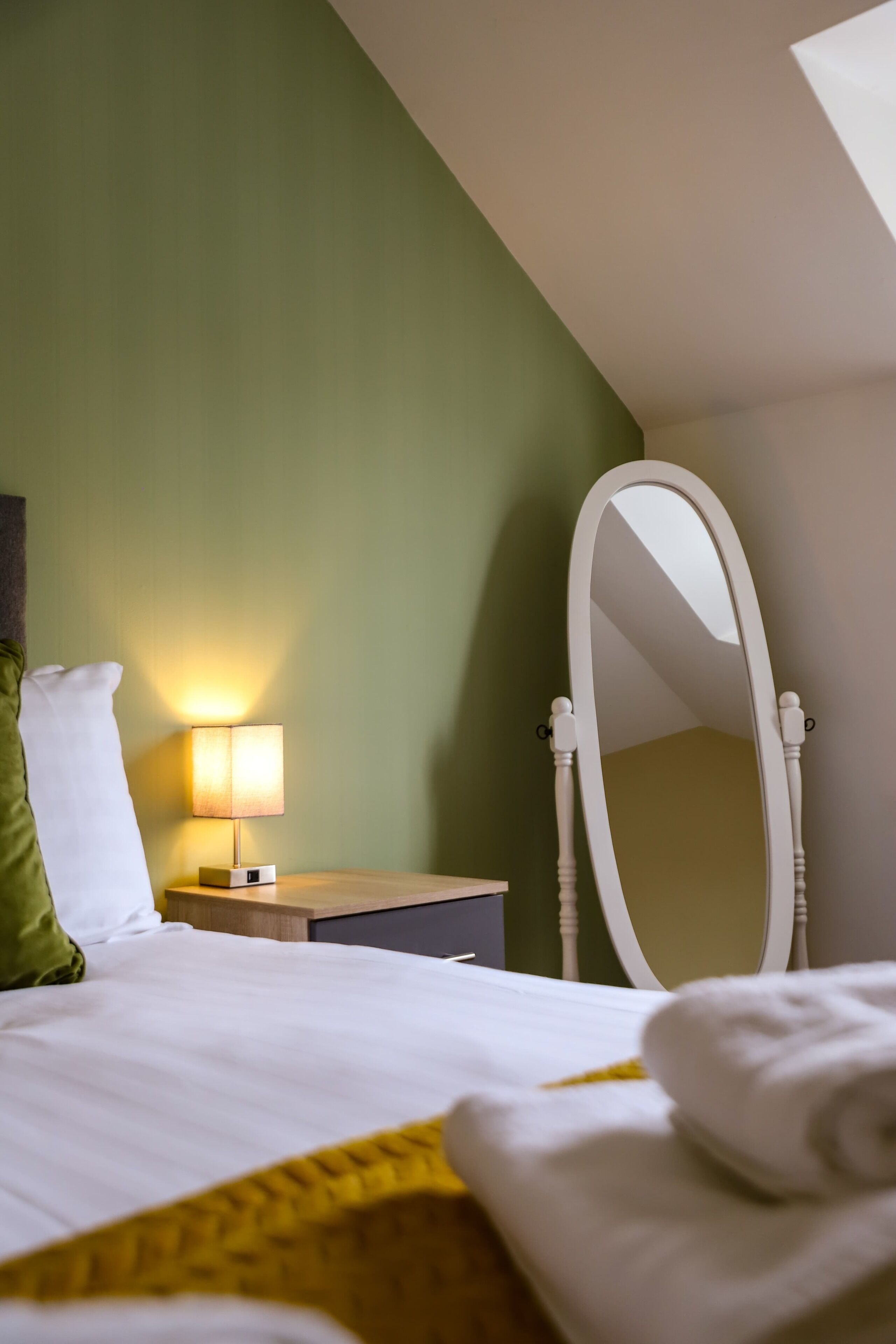 Une chambre d’hôtel avec un lit, une table de chevet avec une lampe, un miroir et un mur vert.