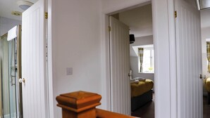 Un pasillo con puertas blancas, una barandilla de madera y un vistazo a un dormitorio con cama y ventana.
