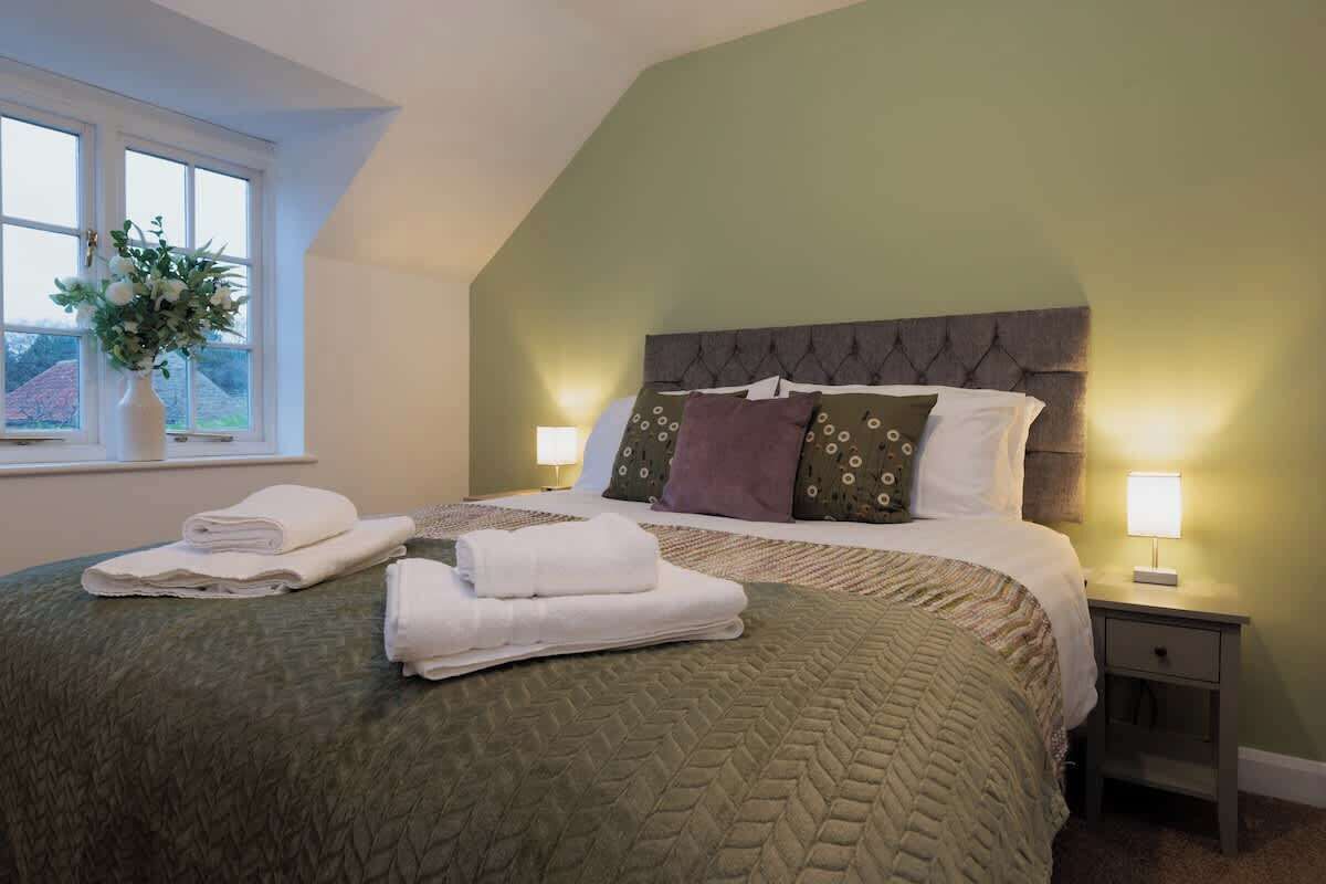 A neatly made bed with pillows and folded towels, a bedside lamp, and a window with a view.