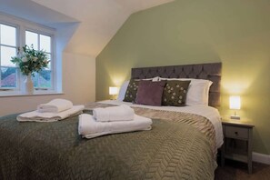 Ein ordentlich bezogenes Bett mit Kissen und gefalteten Handtüchern, eine Nachttischlampe und ein Fenster mit Blick.