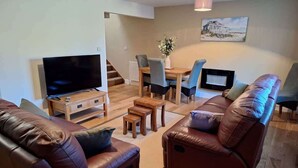 A living room with a TV, leather sofas, a coffee table, and a dining area with chairs and a table.