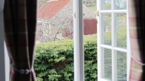 A window with curtains, a view of a red-roofed building, and green foliage.