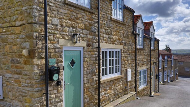 A stone building with a green door, windows, and a visible electrical box.