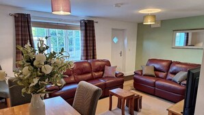 A living room with two leather sofas, a wooden coffee table, a TV, and a vase with flowers.