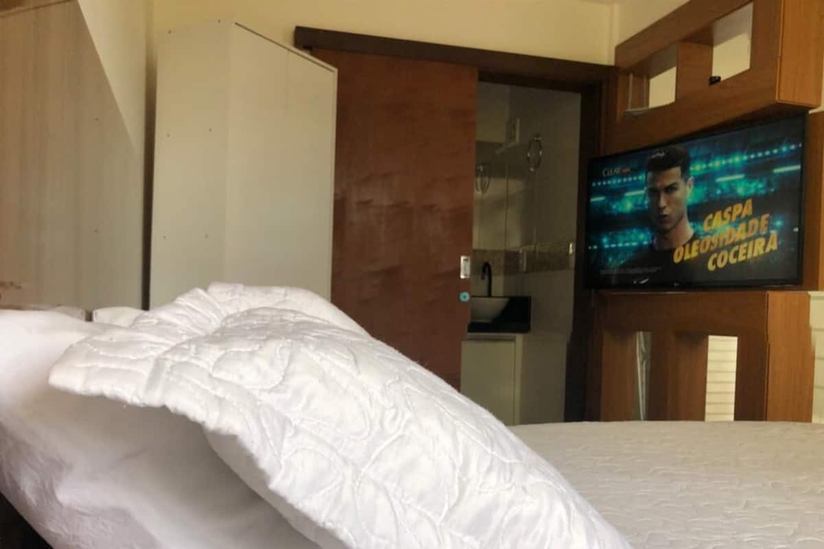 A hotel room with a bed, a television displaying a program, and a wooden wardrobe.