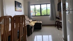 A living room with a sofa, a dining table with chairs, a TV mounted on the wall, and a refrigerator. - Residencial de Aluguel Sol da Villa (Bombinhas)