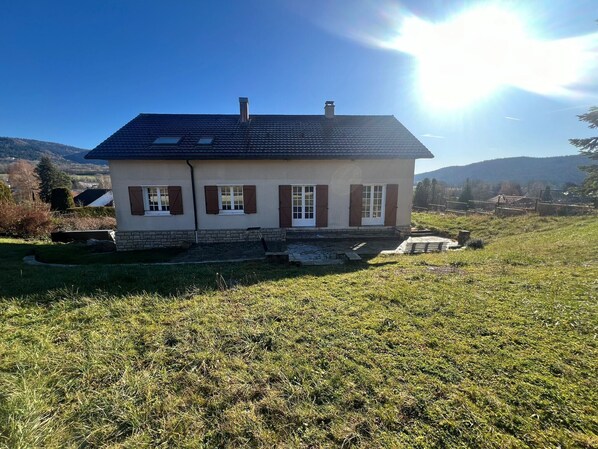 Une maison à deux étages, avec un toit en pente, une cheminée et des fondations en pierre.