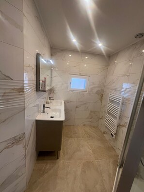 Une salle de bain moderne avec un mur en marbre, un lavabo, un miroir, une fenêtre et un espace douche.