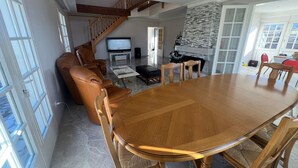 A spacious living room with a wooden dining table, leather chairs, a fireplace, and a staircase leading to an upper floor. - COZY HOME  (Plateau d'Hauteville)