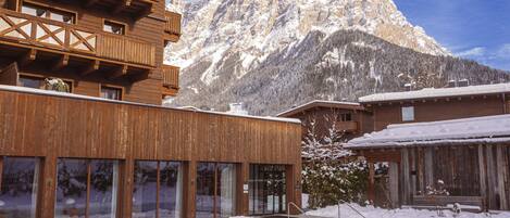 Un edificio in legno con una piscina di fronte, circondato da montagne innevate.
