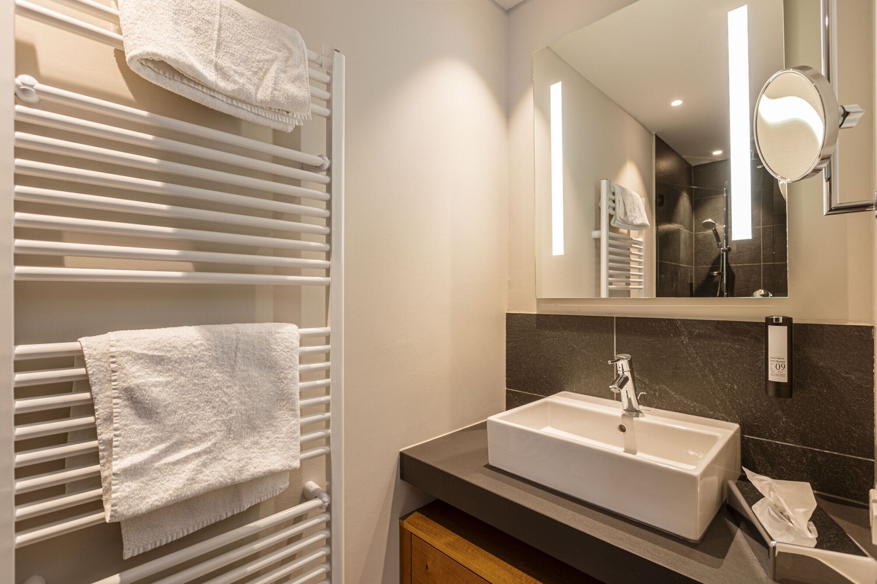 A modern bathroom with a white bathtub, a large mirror, and a towel rack with towels.