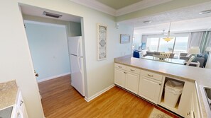 A modern kitchen with white cabinets, a granite countertop, and a view of the living area.