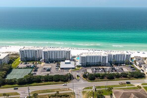 A beachfront hotel with multiple buildings, a parking lot, and a road in the foreground.