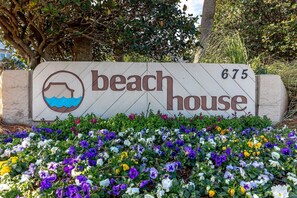 Un panneau indiquant une maison de plage, orné d’un symbole représentant l’eau et entouré de diverses fleurs aux couleurs vives.