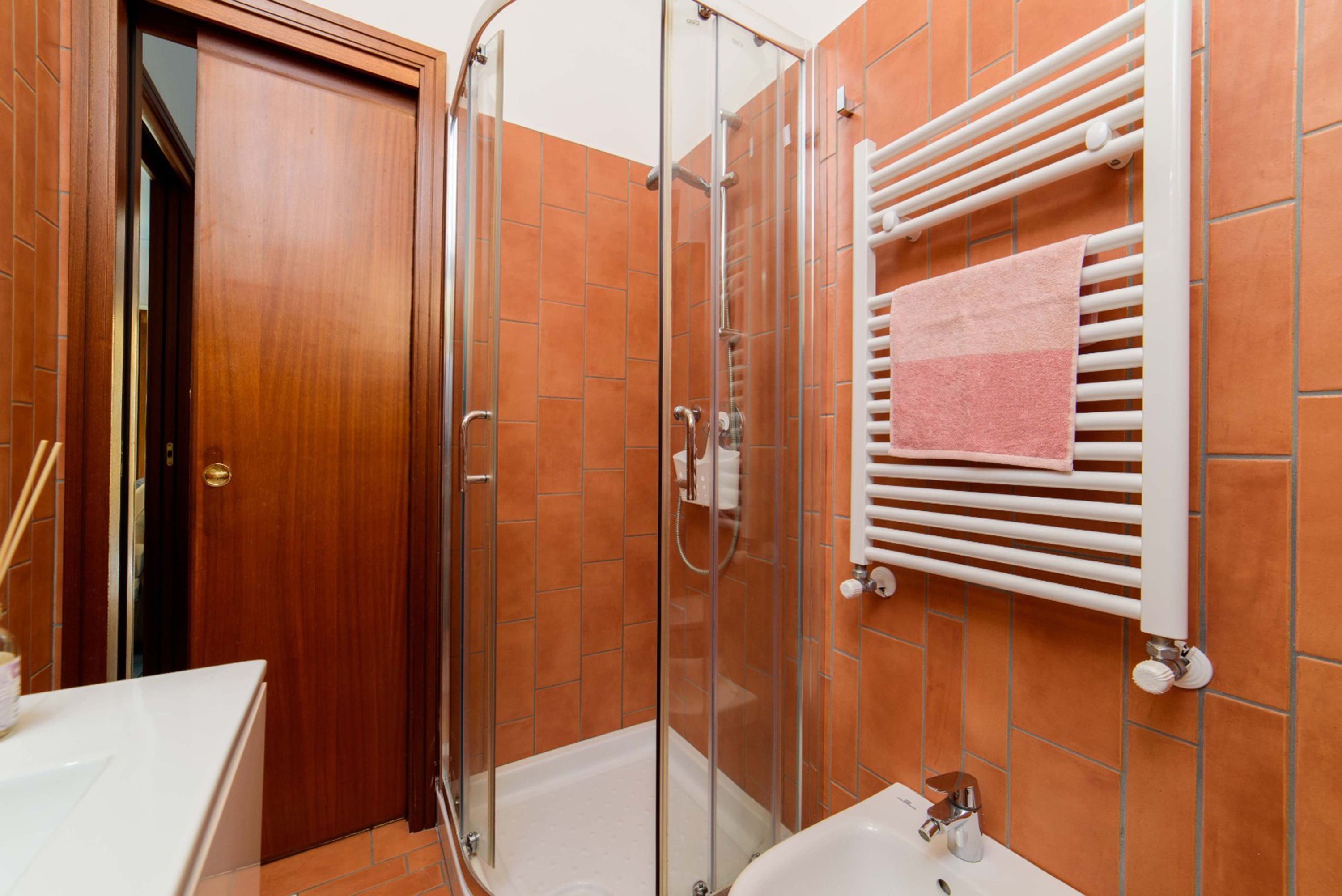 A bathroom with a glass-enclosed shower, a white sink, and a towel rack with a pink towel.