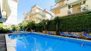 A swimming pool with blue lounge chairs and a stone wall. - Appartamento Sally in Sorrento (Sorrento)
