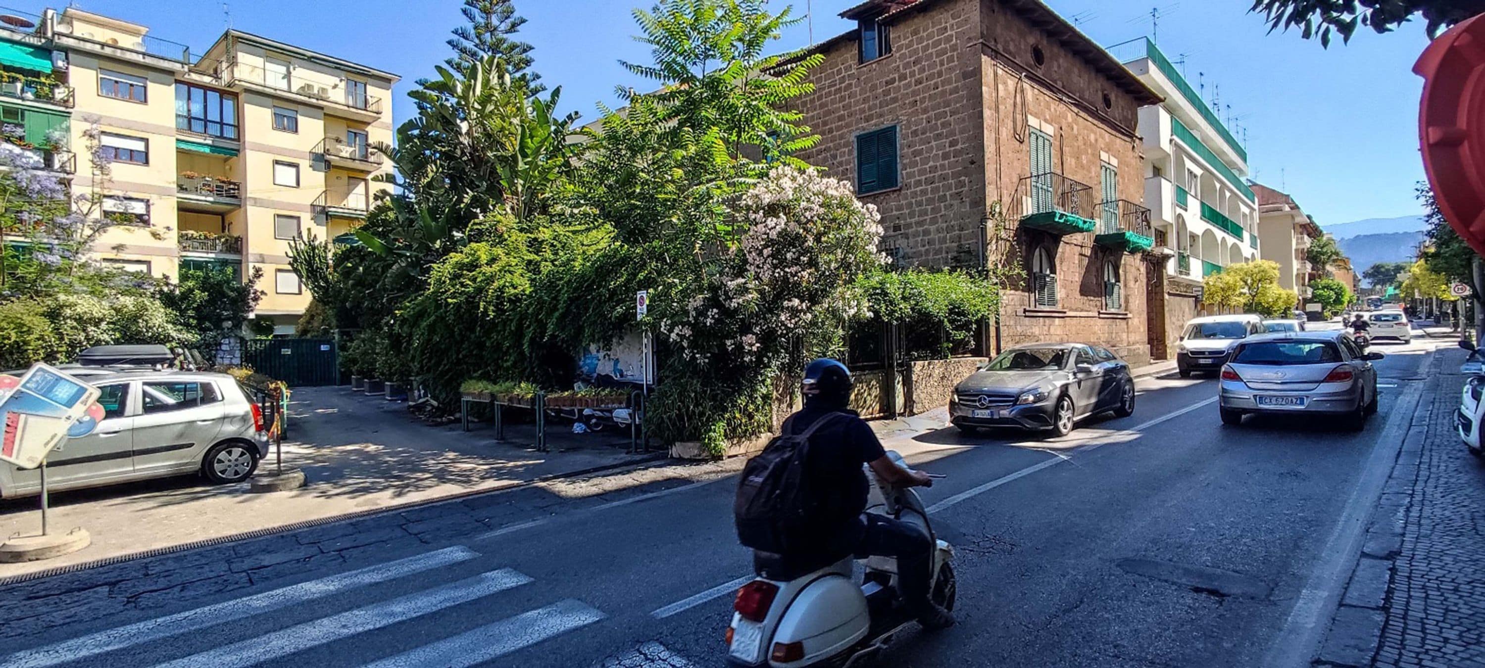 A street scene with parked cars, a motorcyclist, and buildings with balconies.