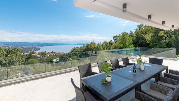 A terrace with a table and chairs, overlooking a scenic view of a lake and distant cityscape. - Luxurious Villa Gabi with an infinity pool and sauna (Mihotici)