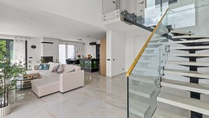 A modern living room with a white sofa, a glass staircase, and a kitchen in the background. - Luxurious Villa Gabi with an infinity pool and sauna (Mihotici)