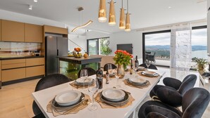 A modern dining area with a long table set for six, featuring gold and white tableware, and a view of the sea through large windows. - Luxurious Villa Gabi with an infinity pool and sauna (Mihotici)