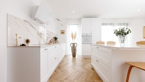 Une cuisine moderne avec des meubles blancs, un pare-feu en marbre et un plancher en bois disposé en motif chevron.