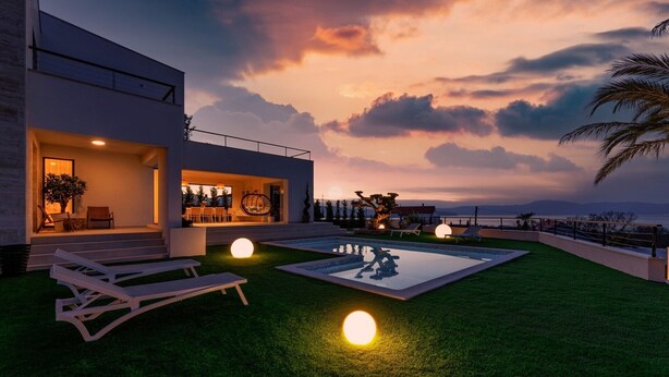 Une maison moderne avec une piscine, un espace salon extérieur et une vue sur la mer au coucher du soleil.