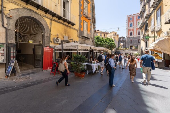 Una calle animada con terrazas de café, un letrero rojo y un gran arco.