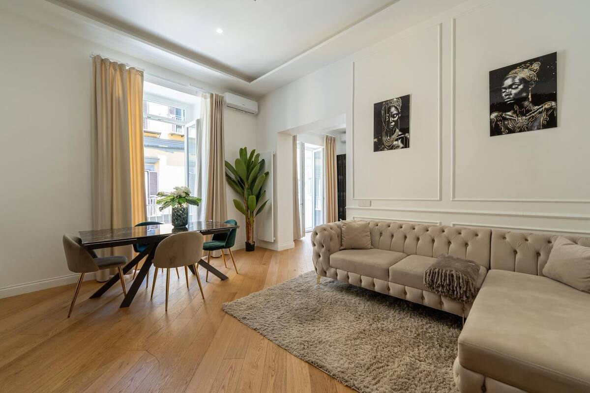 Una sala de estar moderna con un sofá beige, una mesa de comedor con sillas y dos obras de arte en la pared.
