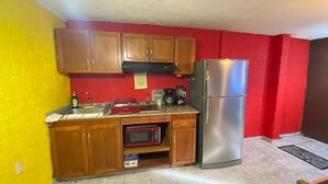 Una cocina compacta con armarios de madera, un refrigerador de acero inoxidable, un microondas y un tostador rojo.