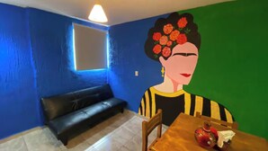 Una habitación con pared azul, un sofá negro, una mesa de madera con un jarrón, y una pared verde con un mural.